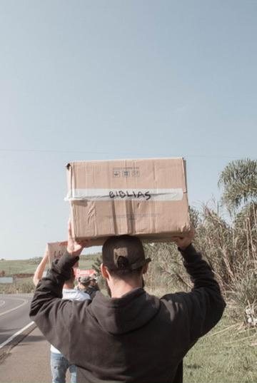 Matheus carregando uma caixa de Bíblias à beira da estrada